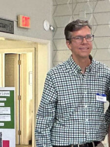 Brian smiling in a checked shirt and name tag at a community event.