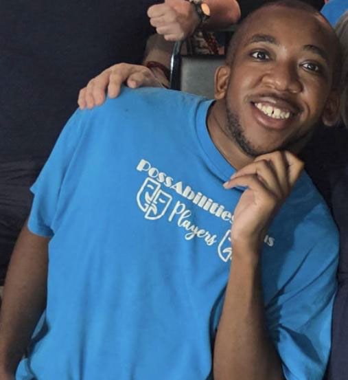 Christopher smiling with his chin on his hand, wearing a blue PossAbilities Players T-shirt.