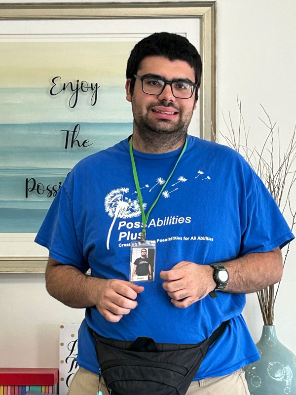 Diego smiling in glasses and a blue PossAbilities Plus T-shirt with a name badge.