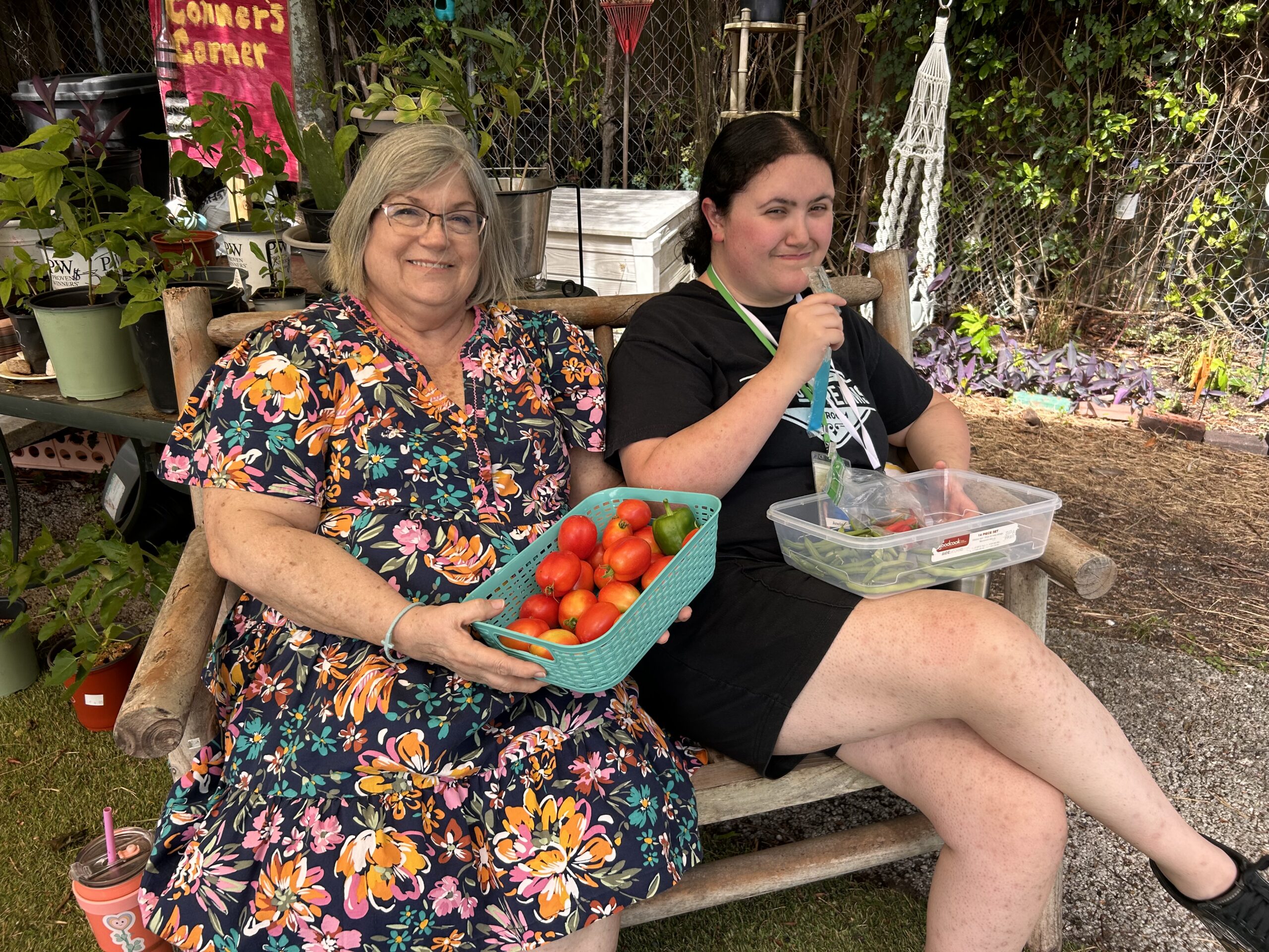 Two women sitting on a bench in The Secret Garden, one holding a basket of freshly picked tomatoes.