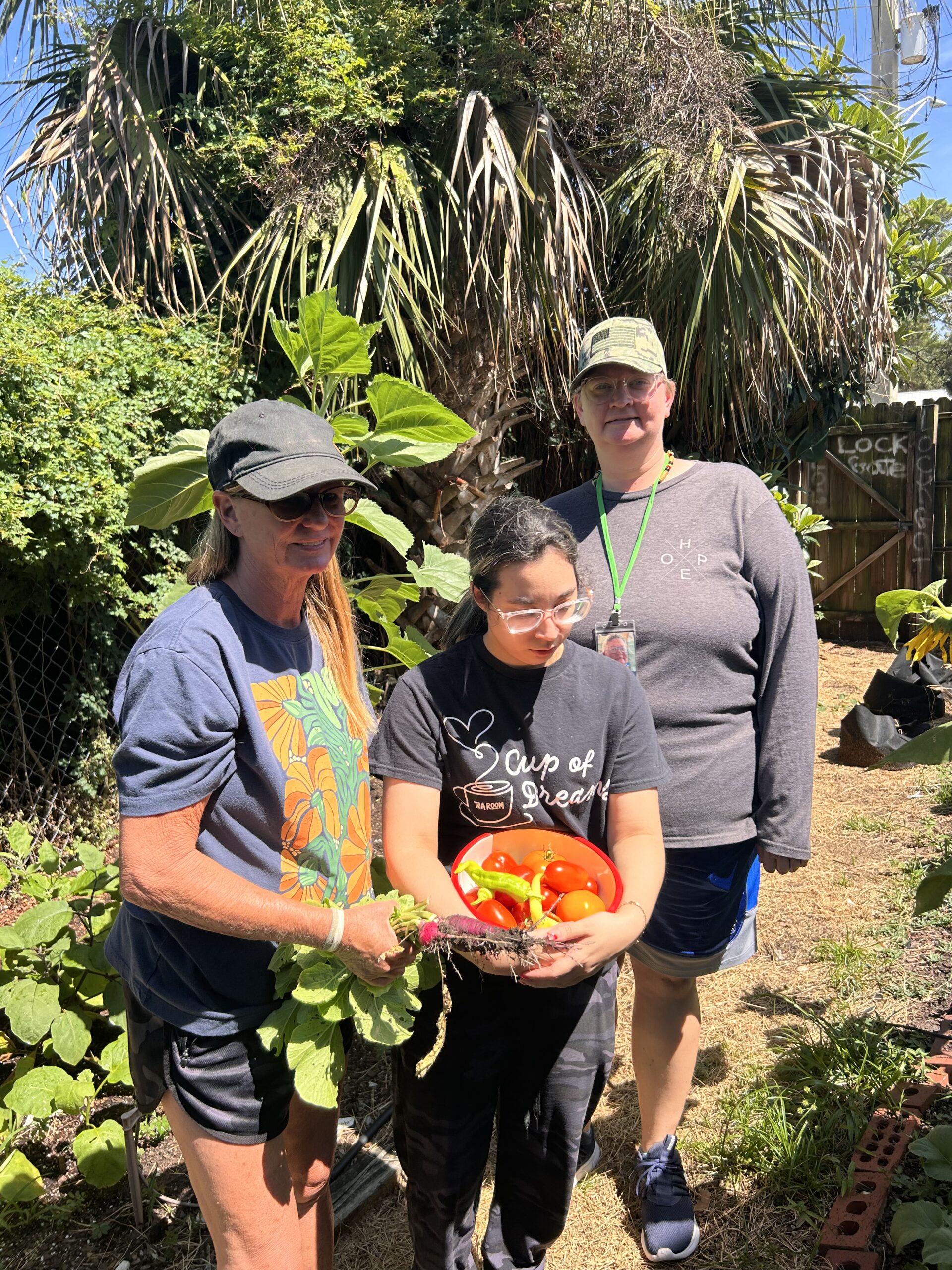 Three gardeners standing among the plants in The Secret Garden, one holding a bowl of freshly picked peppers.