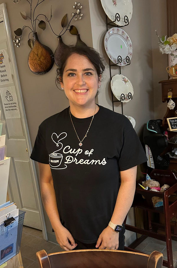 Tamara smiling in a black Cup of Dreams Tearoom T-shirt inside the Tearoom.