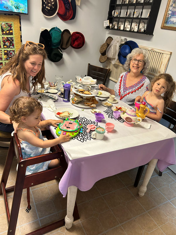 Two women and two young girls enjoying tea, sandwiches and treats at a table in the Cup of Dreams Tearoom.